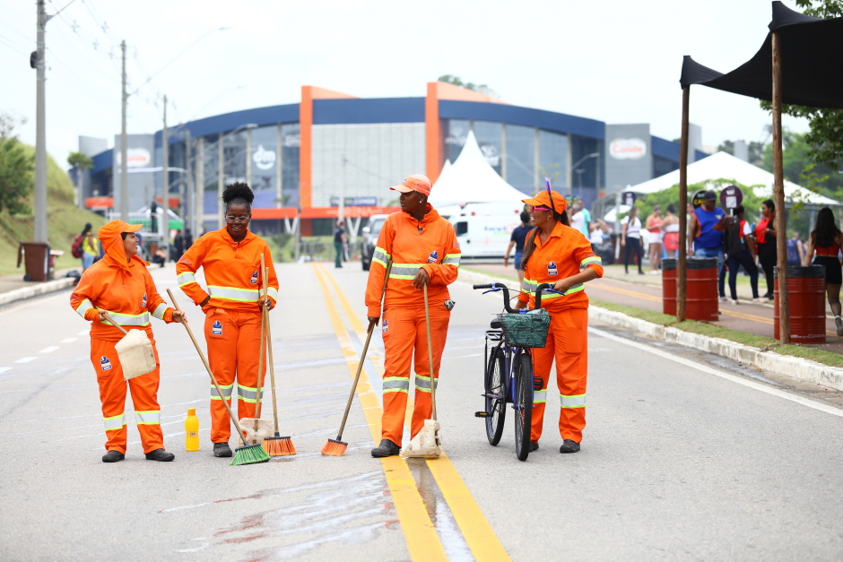 Quatro colaboradoras da equipe de varrição da Urbam aparecem devidamente uniformizadas trabalhando no Carnaval da Via Oeste